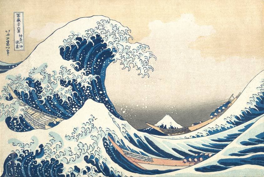 A towering blue wave curls above three narrow boats, with small Mount Fuji visible in the distance beneath its crest.
